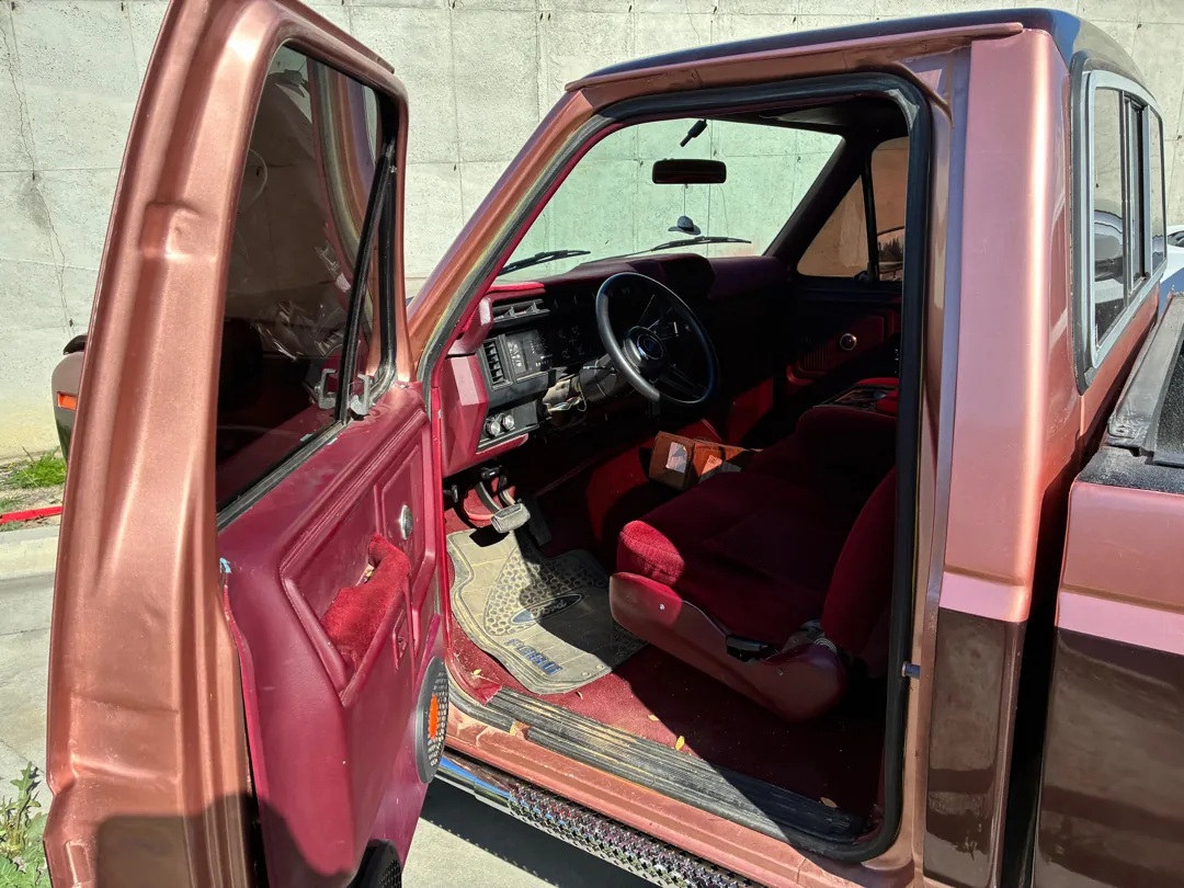 Red cloth interior of an 80s Ford pickup with the door open before an engine swap - Lake Elsinore, CA