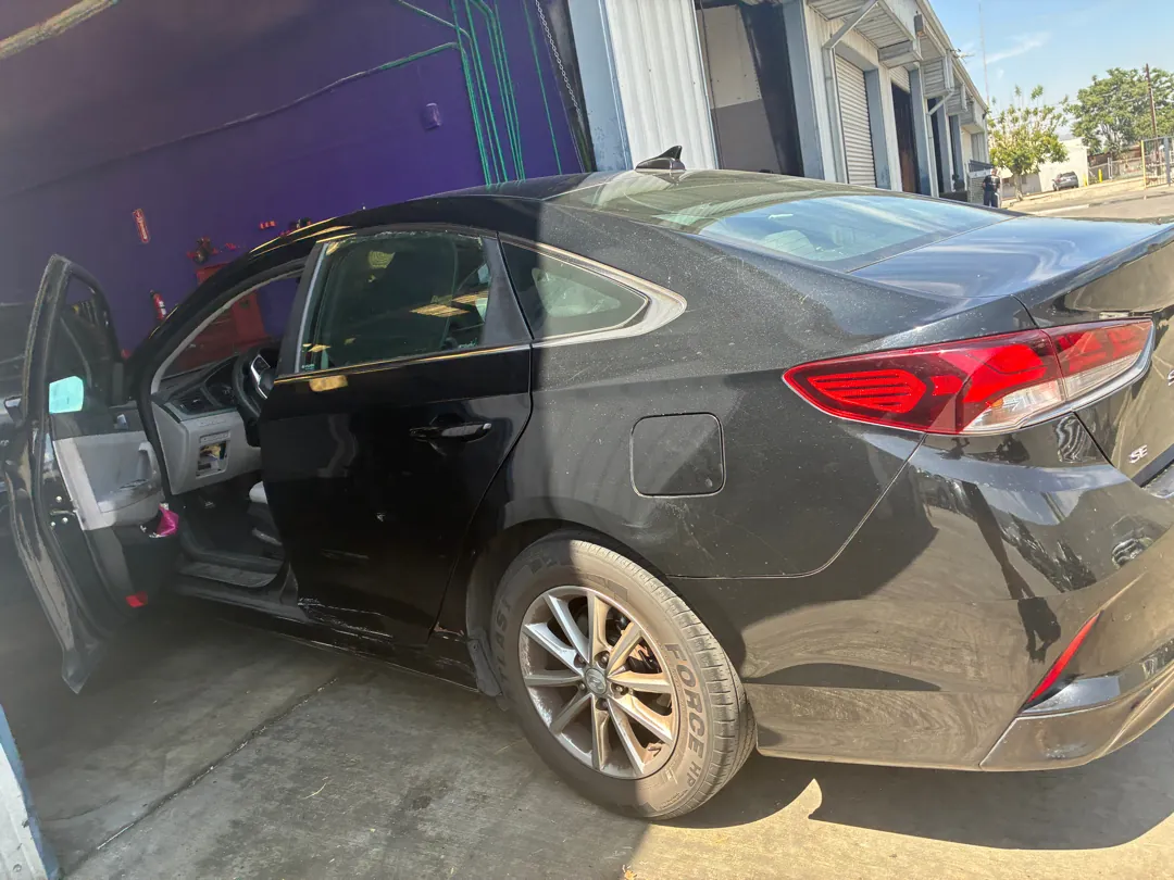 Black Hyundai Sonata with the driver's door open in a shop yard between road tests - Murrieta, CA